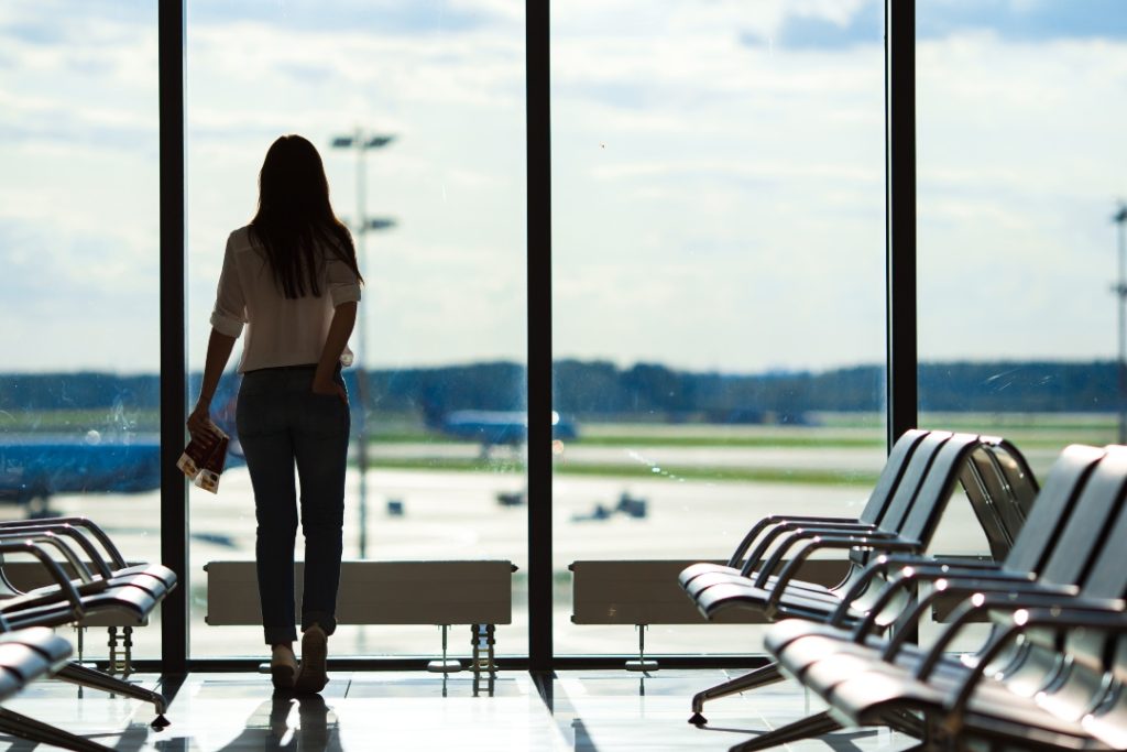 Mulher olhando janela de aeroporto e cogitando tentar um processo contra companhia aérea.