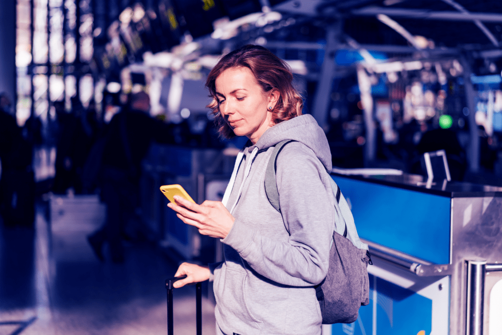 Mulher em aeroporto com celular na mão, resolvendo cancelamento de passagem aérea.