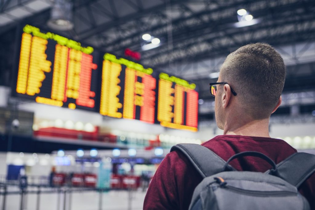 Homem observando em painel em aeroporto que teve o voo cancelado.