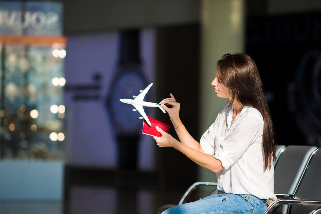 Mulher em aeroporto com visto em mãos e avião de brinquedo para representar o mês do cliente.