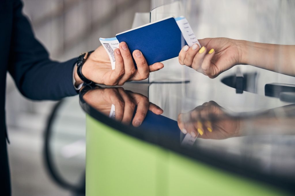 Homem entregando passagem comprada através de skiplagging no balcão de aeroporto.