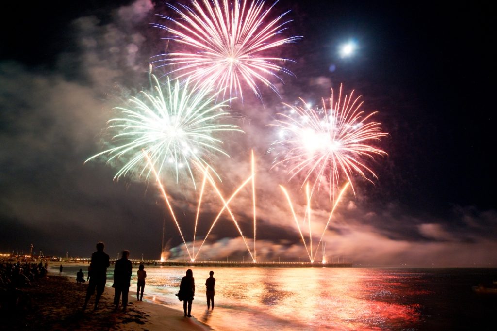 Pessoas assistindo fogos à beira mar em viagem de fim de ano.