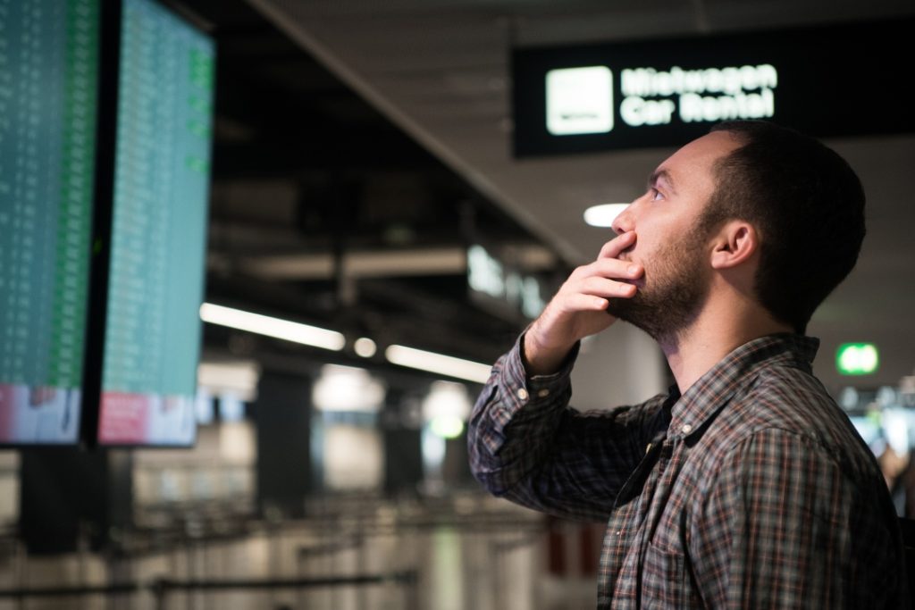 Homem olhando painel e aeroporto com atraso de voo internacional.