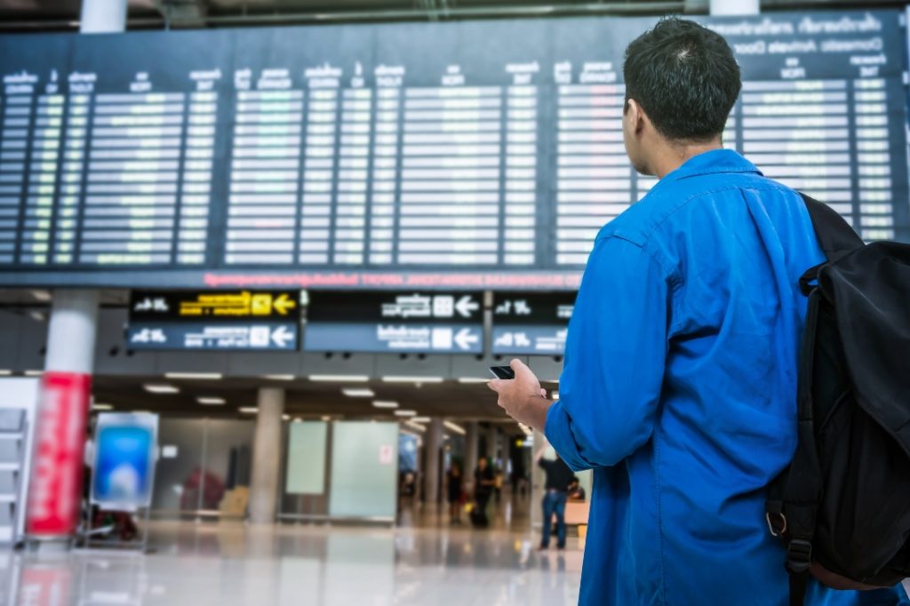 Homem olhando painel de aeroporto vendo a companhia cancelar voo.