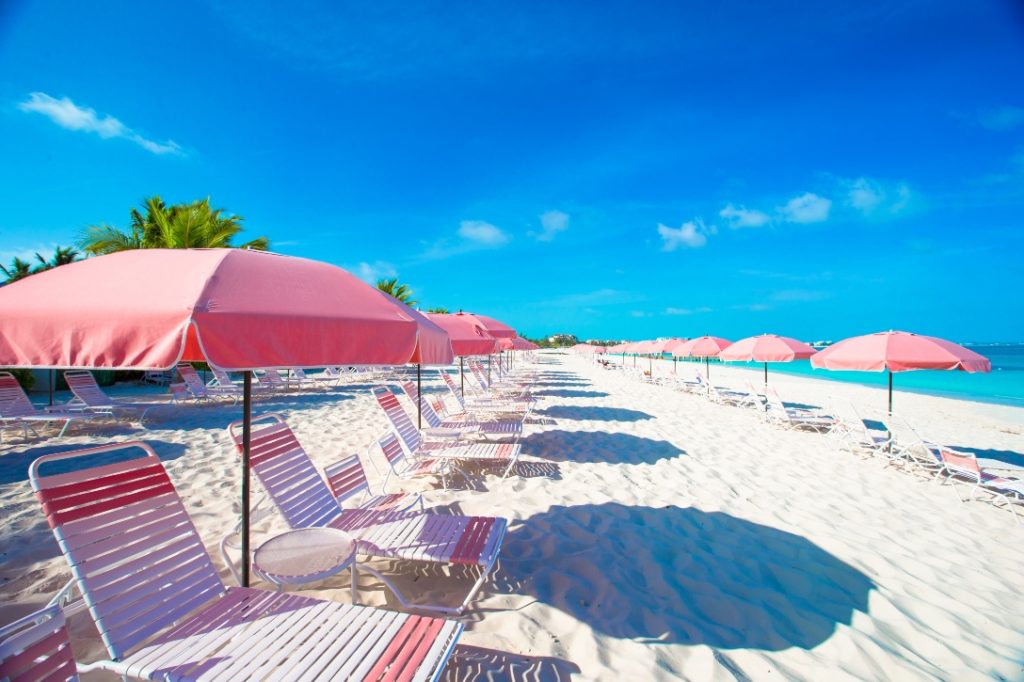 Praia de areia branca com espreguiçadeiras para representar destinos para o verão.